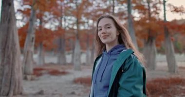 Parkta yürüyen ve kameraya bakan çekici bir kadın. Sonbahar parkındaki insanların portresi. Etkin yaşam biçimi.