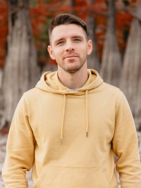 Sonbahar ormanında kameraya bakan yakışıklı bir adam. Sarı kapüşonlu beyaz bir genç.