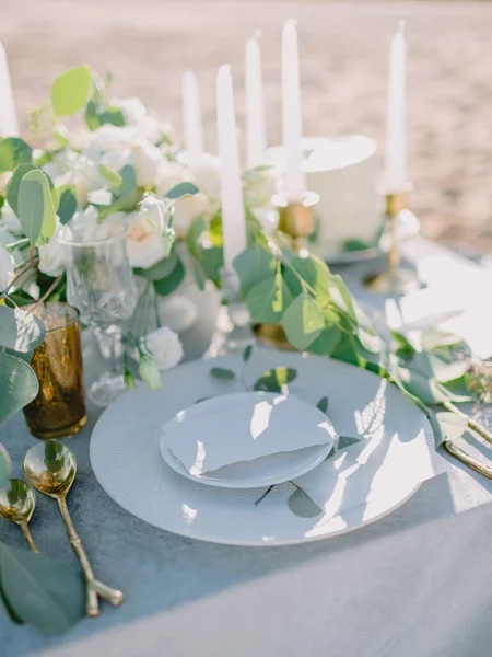 Elegant table setting with a paper card decorated with eucalyptus branches close up. Romantic table with paper invitation card. Wedding Mockup.