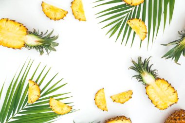 Beyaz arka planda dilimlenmiş ananas ve palmiye yapraklarından yapılmış tropik bir çerçeve. Düz yatış, üst görünüm.