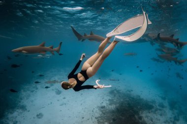 Genç bir kadın Maldivler 'de hemşire köpekbalıklarıyla berrak bir tropikal suda şnorkelle yüzüyor.