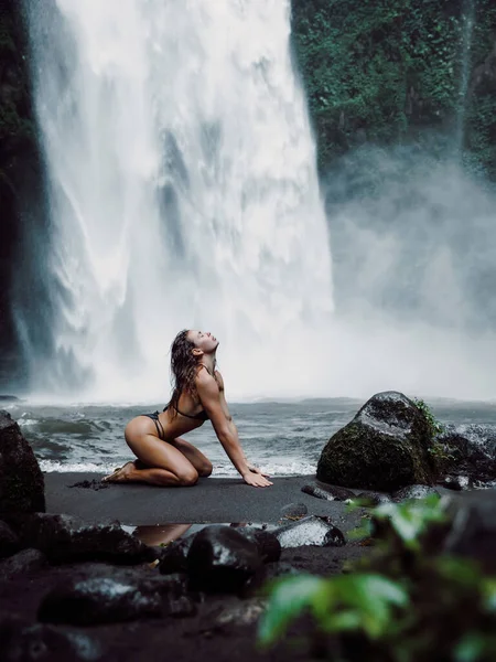 Young woman in swimsuit posing near powerful waterfall. Traveler girl on waterfall in Bali