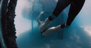 Mavi denizde serbest dalış yapan kadın. Dişi, iskelenin altında yüzgeçleriyle yüzüyor. Yüksek kalite 4k görüntü