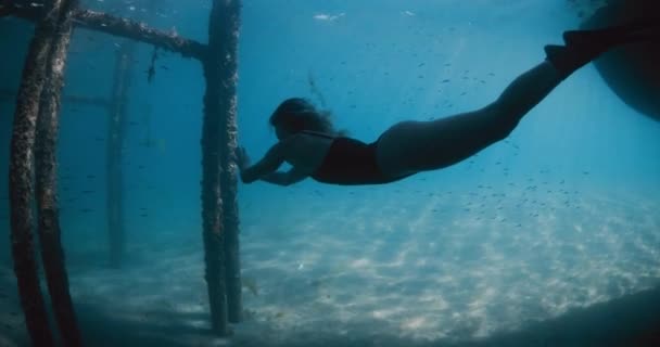 女性は青い海で水中を泳いでいた 女性はピアの下でフィンで泳いでいます 高品質の4K映像 — ストック動画