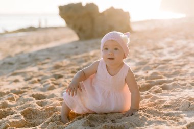 Açık havada gün batımında güzel bir kız. Okyanus sahilinde pembe elbiseli bebek.