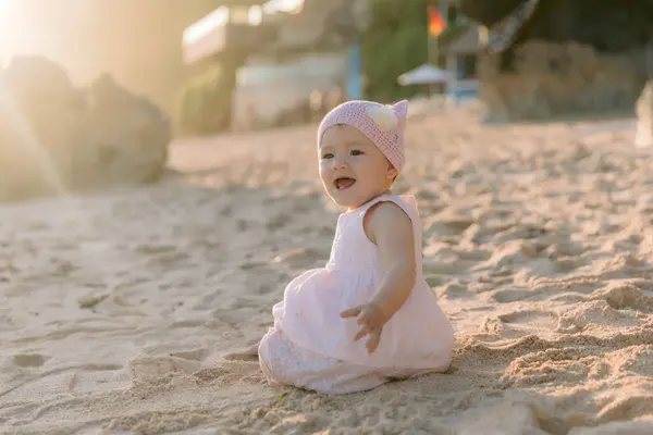 快乐的微笑着美丽的女孩在沙滩上与夕阳西下 穿着粉红衣服的婴儿 — 图库照片