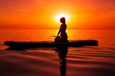 Denizde, gün batımında ya da gündoğumunda, kürek çeken bir kadın..