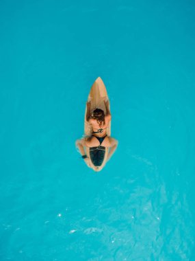 Mavi okyanusta sörf tahtasında oturan bikinili seksi kız. Hava görünümü