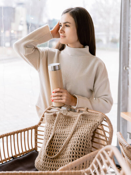 Молодая привлекательная женщина с термосом расслабляющий в кафе