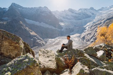 Adam en yüksek dağlardaki kayalarda dinleniyor ve oturuyor. Buzul ve turist dolu bir dağ.