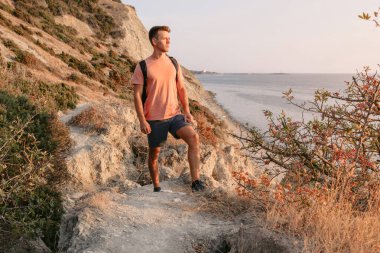 Sırt çantalı gezgin sıcak güneş ışığıyla okyanus kıyısında yürüyor..