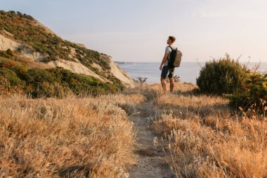 Tişörtlü ve şortlu bir gezgin akşam sahilde sırt çantalı..