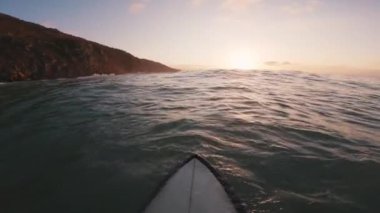Sıcak günbatımında okyanusta sörf tahtasında oturan sörfçü. Okyanusta sörf yapmanın birinci şahıs görüntüsü. Yüksek kalite 4k görüntü