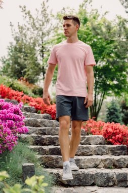 Yakışıklı sıska adam yaz parkında merdivenlerde yürüyor..