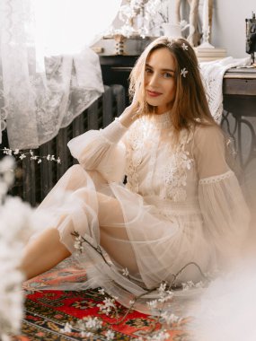Eski moda gelinlik giyen genç, şık bir model evde, eski moda iç mekanda oturuyor.