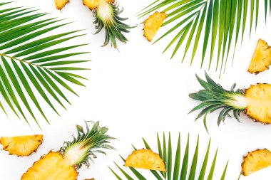Beyaz arka planda dilimlenmiş ananas ve palmiye yaprakları olan tropik bir çerçeve. Düz yatış, üst görünüm.