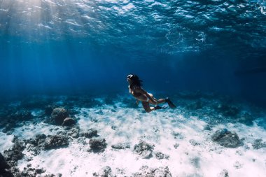 Freediver mavi okyanusta güneş ışınlarıyla suyun altında süzülür.