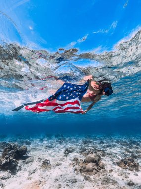 Kadın, tropikal mavi okyanusta Amerikan bayrağıyla su altında yüzüyor. Bağımsızlık Günü kavramı.