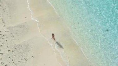 Okyanus kumsalında koşan bir kadın. Tatildeki bir kızla birlikte havadan aşağı manzara. Yüksek kalite 4k görüntü