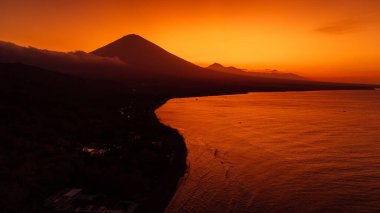 Panoramik insansız hava aracı Bali 'de volkan ve günbatımı ile kıyı şeridini görüyor..