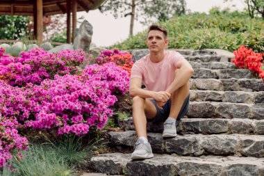 Yazın çiçek açan bahçede merdivenlerde oturan yakışıklı beyaz adam..