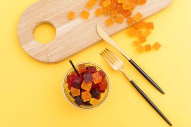 Tahta bir tabakta, çatal, çatal ve bıçakla lezzetli meyveli jöle. Sarı arkaplan