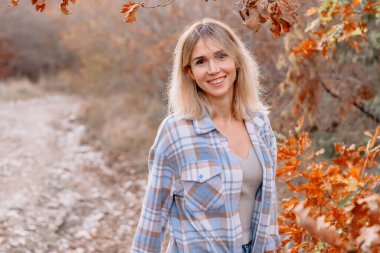 Sonbahar ormanlarındaki neşeli sarışın kadın portresi ya da sıcak güneş ışığı olan park.