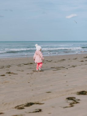 Küçük bir kız çocuğu okyanus kıyısında yürüyor. Kış açık hava konsepti.