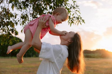Mutlu anne küçük kızıyla dışarıda gün batımı tonlarıyla oynuyor.