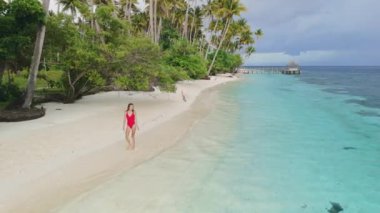 Mayo giyen kadın sakin mavi denizli tropikal kumlu sahilde yürüyor. Palmiye ağaçları ve dişilerle drone görüntüsü. Yüksek kalite 4k görüntü
