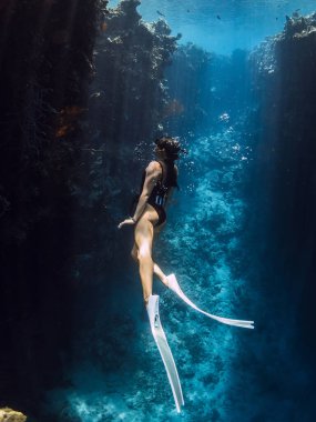 Freediver kızı, Menjangan 'daki mavi okyanusta, resif kayalarının yanında su altında yüzüyor. Tropikal denizde güneş ışınlarıyla serbest dalış