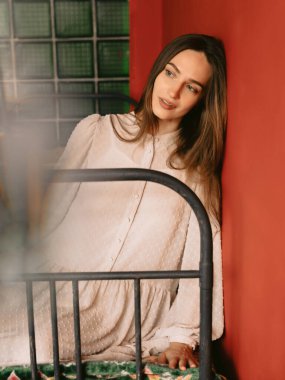 Çekici, kusursuz ciltli, antika bir elbise giyen, retro yatakta oturan genç bir kadın. Moda konsepti