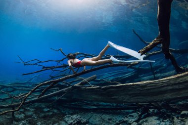 Freediver beauty woman glides and posing with fins over sunken logs in the lake. Free diving in blue crystal lake clipart