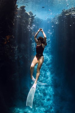 Freediver kadın Menjangan 'daki mavi okyanusta resif kayalarının altında poz veriyor. Kadınlarla serbest dalış