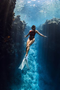 Serbest dalgıç kadın Menjangan 'daki mavi okyanusta kayalıkların altında poz veriyor..