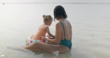 Anne, küçük kızıyla tropik okyanus sahillerinde oynuyor. Sahil şeridindeki güzel mutlu aile. Yüksek kalite 4k görüntü