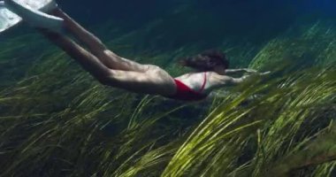 Seksi serbest dalgıç kadın, şeffaf gölde suyun altında yüzüyor.