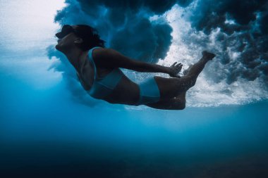 Okyanus dalgası altında sörf tahtası olmayan bikinili bir kadın. Çarpışan dalganın altında ördek dalışı