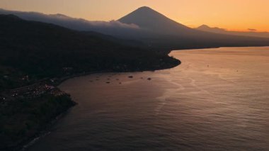 Tekneli okyanus ve volkanik dağlı kıyı şeridi, Amed, Bali 'de sıcak, parlak günbatımı. İHA görüntüsü. Yüksek kalite 4k görüntü