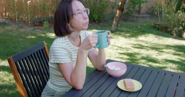 Kadın arka bahçede içki içip yemek yiyor.