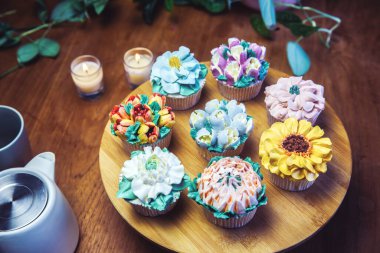 Various cupcakes decorated with colorful flower icing on wooden table, floral bouquet, wedding cake, High tea, Holiday concept Mothers day