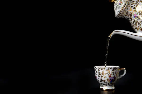 Pouring hot tea in vintage cup on black background, liquid movement in a cup, Antique crockery with copy space cozy high tea concept
