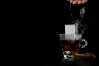 Glass of hot tea with tea bag hanging black background copy space, and cinnamon stick