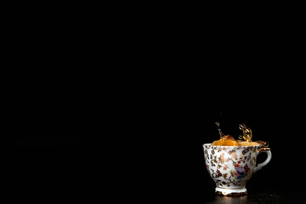 stock image Splash in vintage cup of black tea isolated on black background with delicious cookies, copy space detox healthy medicine herb