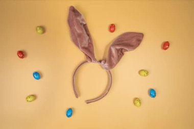 Movement of multicolour Easter eggs on a orange background with bunny ears. Happy Easter. rolling in one direction. Concept of traditional spring celebration. Symbol of new life. top view
