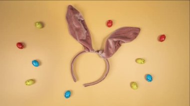 Movement of multicolour Easter eggs on a orange background with bunny ears. Happy Easter. rolling in one direction. Concept of traditional spring celebration. Symbol of new life. top view Holiday