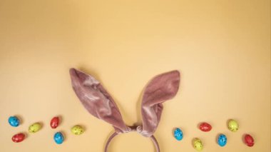 Movement of multicolour Easter eggs on a orange background with bunny ears. Happy Easter. rolling in one direction. Concept of traditional spring celebration. Symbol of new life. top view Holiday