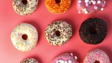 Various freshly colorful delicious sweet donuts in a row. Stop motion. Donuts of different moving, Four glazed sweet donuts. Bakery and food concept. Top view. Chocolate, pink, blue donuts in pack. 4K, UHD top view pink background turning