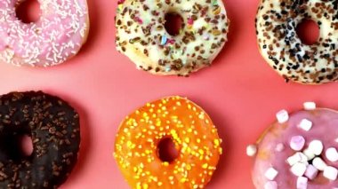 Various freshly colorful delicious sweet donuts in a row. Stop motion. Donuts of different moving, Four glazed sweet donuts. Bakery and food concept. Top view. Chocolate, pink, blue donuts in pack. 4K, UHD top view pink background turning