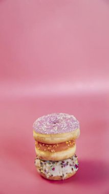 Sweet doughnuts stacked on top of each other in the form of a tower, vertical video donuts tasty delicious sweet candy snack on pink background